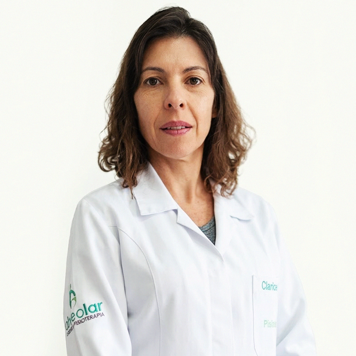 Retrato de plano médio da Professora Clarissa Maria de Pinho Matos. Ela possui cabelos castanhos ondulados na altura dos ombros e veste um jaleco branco. Na manga direita do jaleco, há um logotipo verde com o texto "Alveolar Cursos e Fisioterapia". No bolso esquerdo, nota-se o nome "Clarice" bordado em verde. O fundo é branco e neutro.