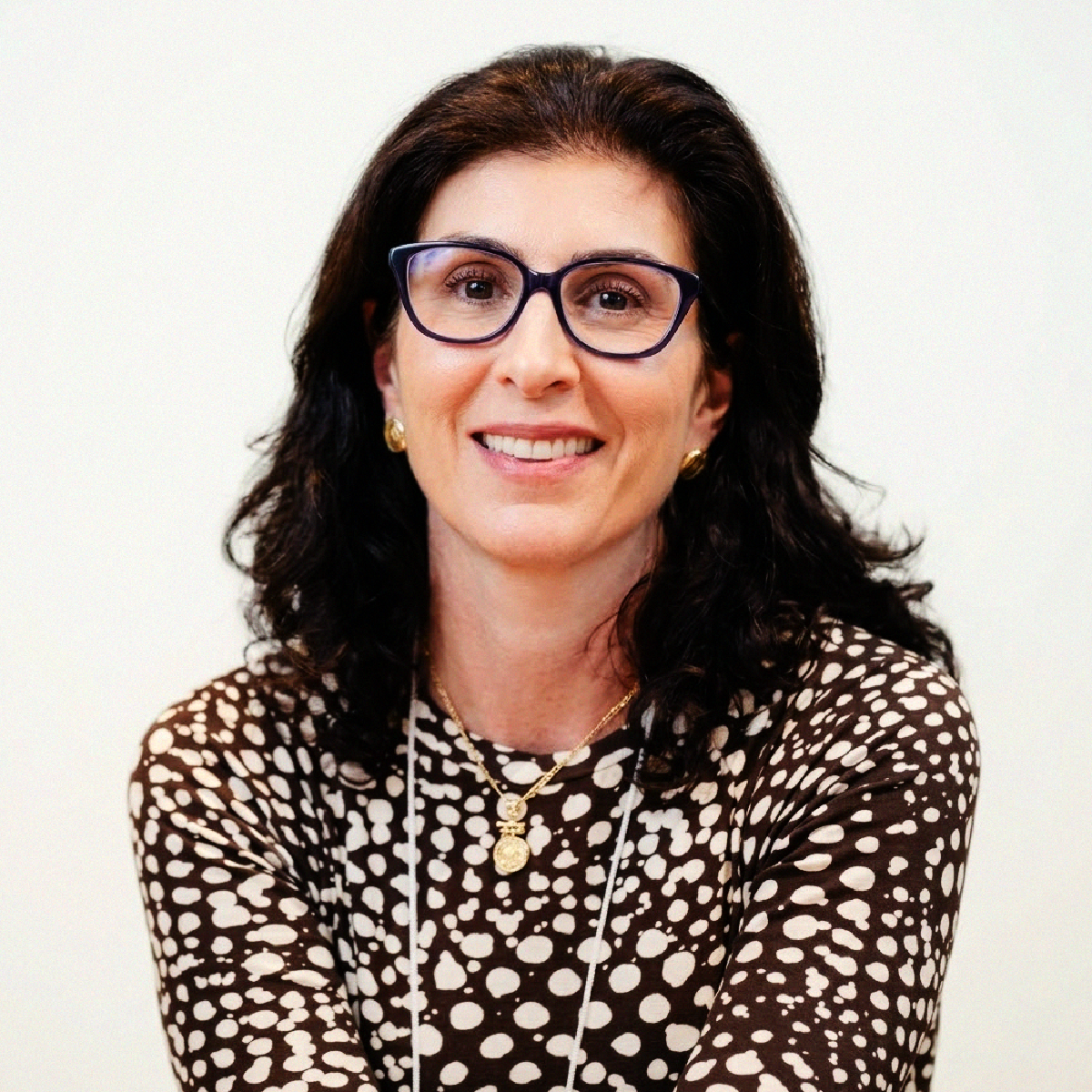 Retrato profissional da Profa. Cristina Said Saleme sorrindo, de óculos, cabelos castanhos ondulados e blusa preta com bolinhas brancas.