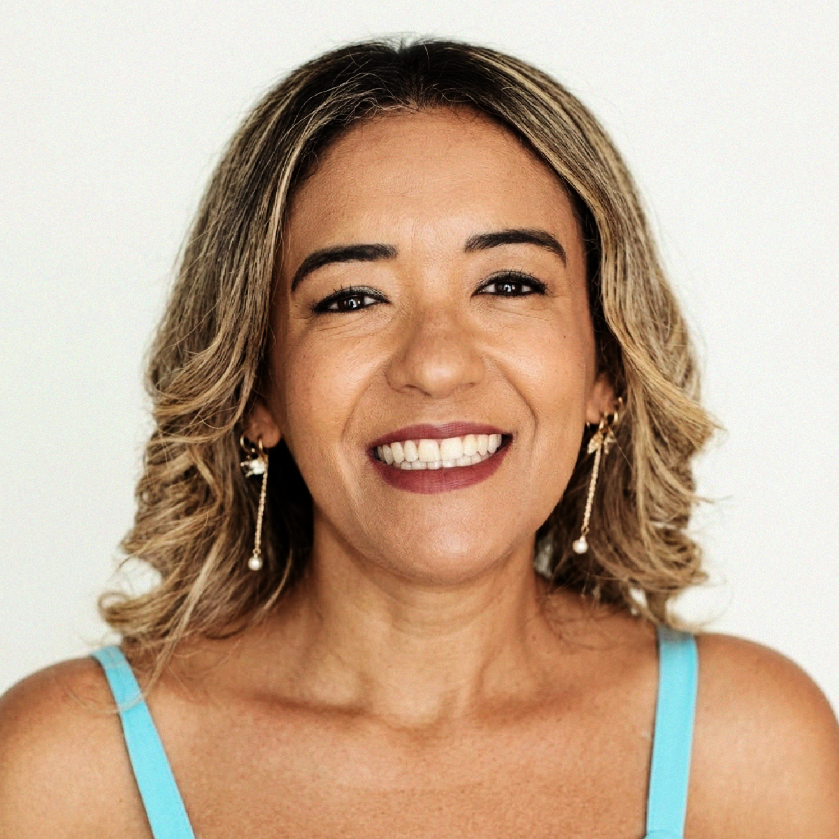 Retrato da Profa. Daniela Corrêa sorrindo, de cabelos loiros ondulados, blusa de alça azul-clara e brincos longos.