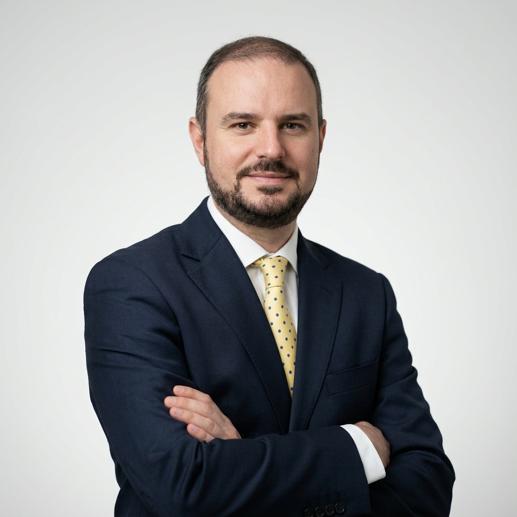 Retrato do professor Eduardo Batista Cândido, com cabelos curtos castanhos, barba e expressão levemente sorridente. Veste terno azul-marinho, camisa branca e gravata amarela com pequenas estampas azuis, com os braços cruzados diante de fundo claro.