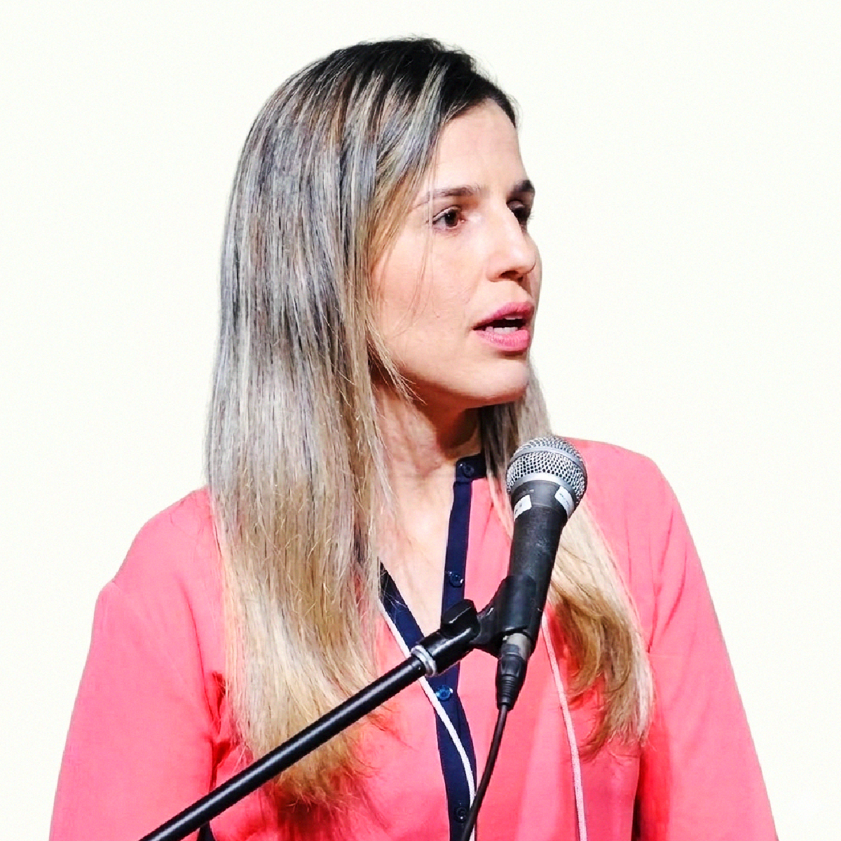 Retrato profissional da Dra. Érika de Oliveira Hansen, com cabelos longos loiros, falando ao microfone.