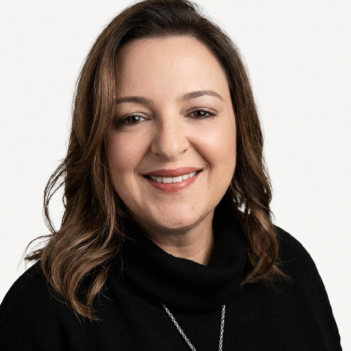 Fotografia de rosto (headshot) da Dra. Juliana Magalhães Machado Barbosa, professora e fisioterapeuta. Ela possui pele clara, cabelos castanhos ondulados na altura dos ombros e sorri para a câmera. Veste uma blusa preta de gola alta e um colar de corrente prateada fina. O fundo é branco liso, com iluminação clara e uniforme que destaca seu rosto.