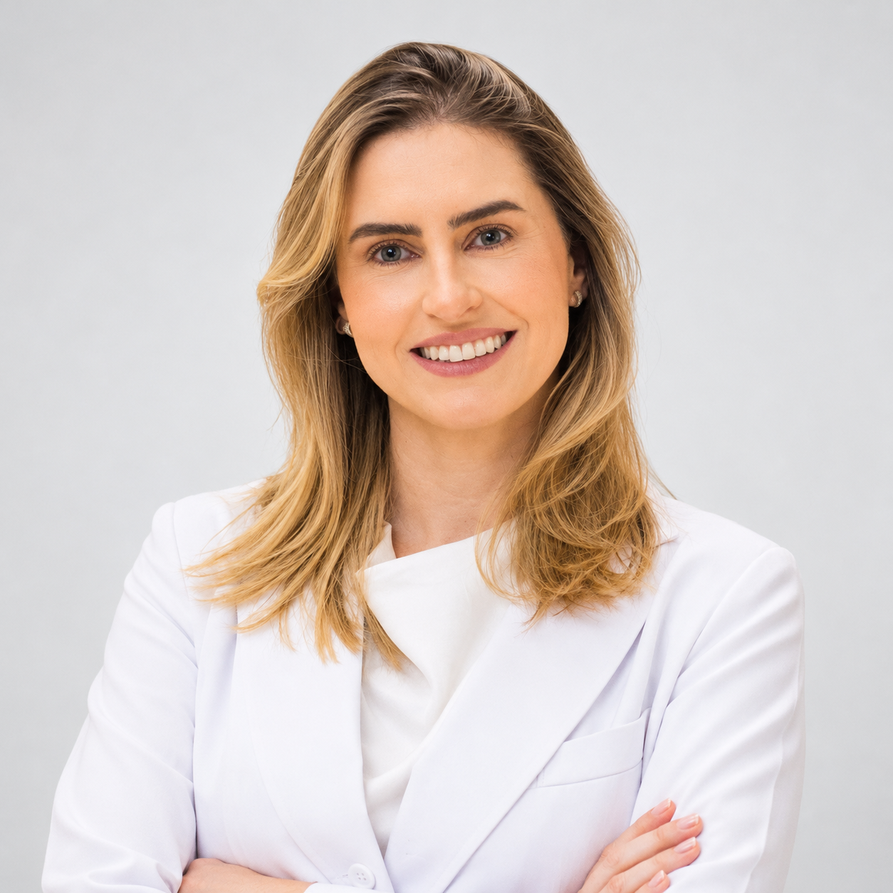 Retrato institucional de Natalia Maria Valenzi Amorim, médica ginecologista e coordenadora da Pós-graduação em Vídeo Histeroscopia da FCM-MG. Possui cabelos loiros na altura dos ombros, veste jaleco branco e aparece sorrindo, com os braços cruzados, diante de fundo cinza-claro.