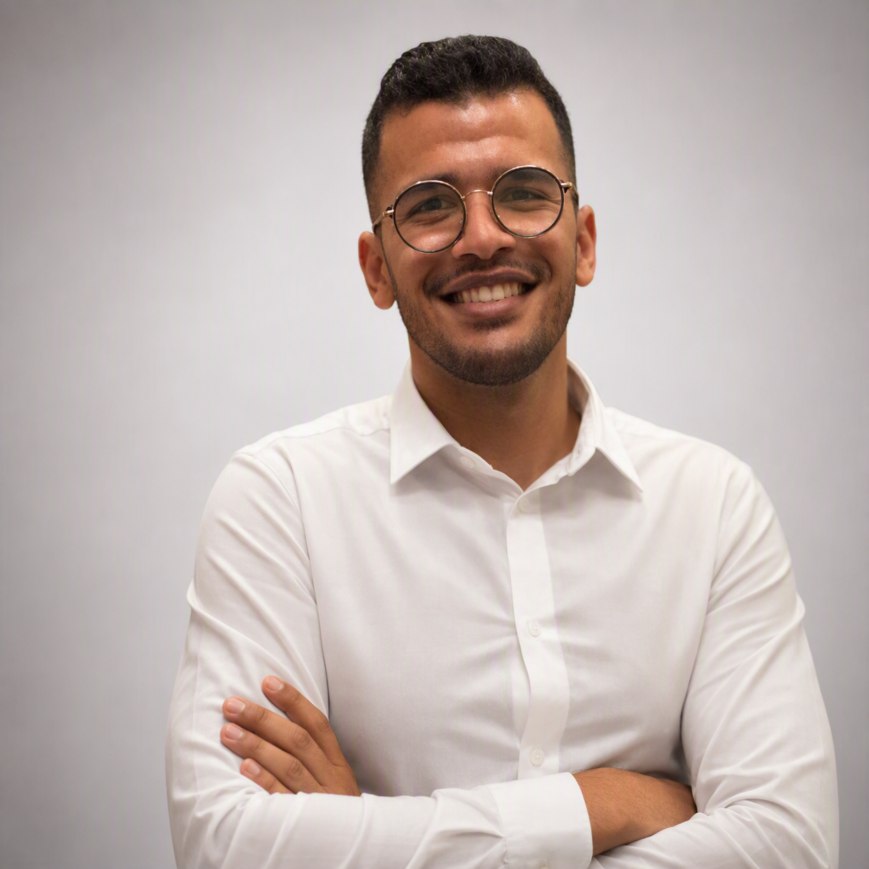 Retrato do professor Ricardo Rodrigues de Sousa Junior, sorrindo, com camisa branca e óculos, em fundo claro.