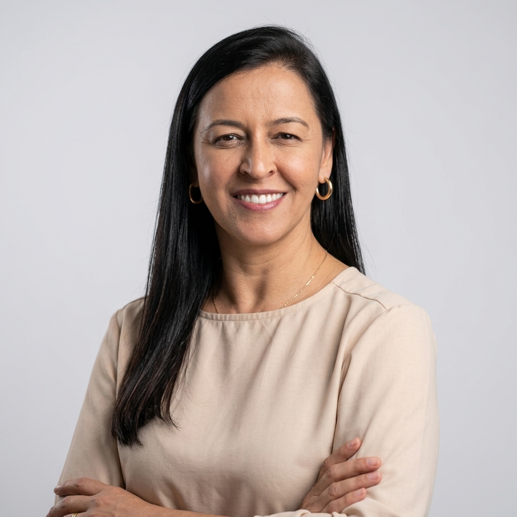Retrato da professora Simone Nascimento Santos Ribeiro, mulher de cabelos pretos, longos e lisos, vestindo blusa bege e brincos dourados. Aparece com os braços cruzados, sorrindo para a câmera, diante de um fundo cinza-claro.