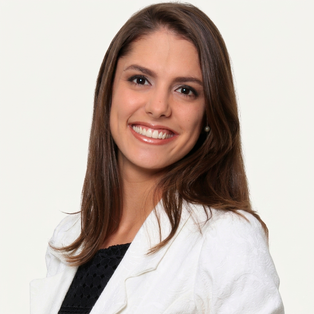 Fotografia de estúdio em plano médio de Laiss Bertola de Moura Ricardo, coordenadora da FCM-MG. Ela é uma mulher jovem com pele clara, cabelos castanhos longos e lisos, e está sorrindo diretamente para a câmera. Veste um blazer texturizado branco sobre uma blusa preta trabalhada em renda. O fundo da imagem é liso, em um tom off-white neutro, com iluminação frontal suave e profissional.